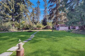 A well-maintained lawn with a stone pathway leading to a building, surrounded by dense trees.