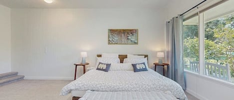 Una camera da letto con un letto grande, due comodini con lampade, una panca, una finestra con vista su del verde e un quadro appeso al muro.