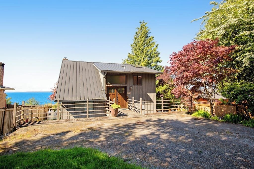 A single-story building with a sloped roof, a wooden fence, and a gravel driveway leading to a wooden door.