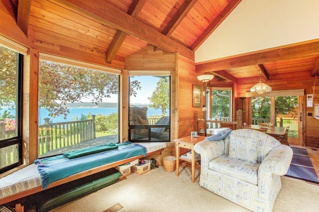 A cozy cabin with a wooden interior, a sofa, a table, and large windows offering a view of the outdoors.