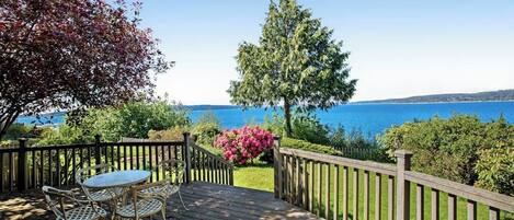 Un terrazzo in legno con tavolo e sedie, affacciato su uno specchio d'acqua e un cielo sereno.