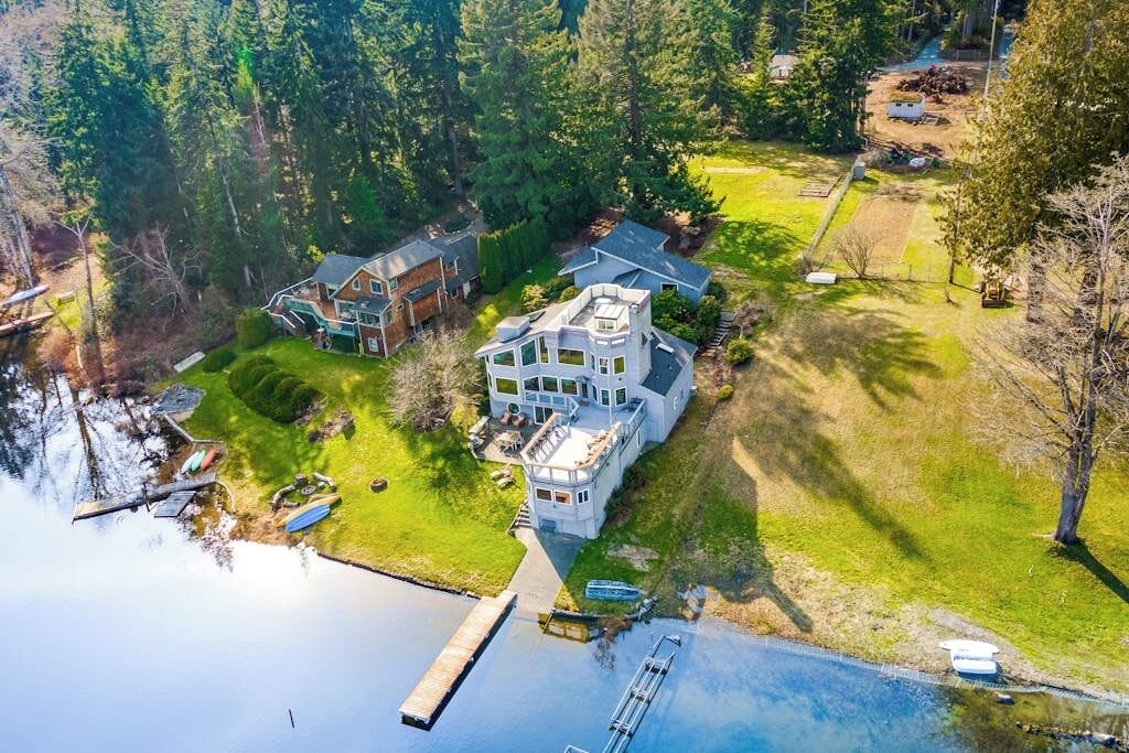 Een groot huis met een aanlegsteiger en een klein bootje, omringd door bebossing en een waterpartij.