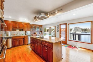 A modern kitchen with wooden cabinets, a central island, and large windows offering a view of a dock and water.
