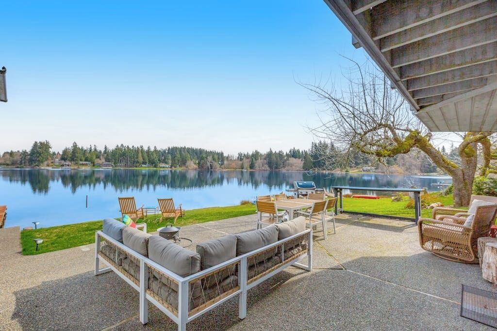 Une terrasse au bord du lac, aménagée avec du mobilier d’extérieur et un barbecue, offrant une vue sur le lac.