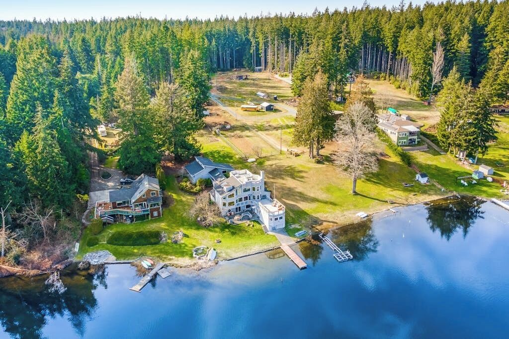 A large house with a dock extending into a lake, surrounded by dense forest.