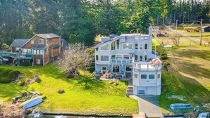 A multi-story house with a dock extending into a body of water, surrounded by a grassy yard and trees. - 4 BR Pet Friendly Waterfront Home with Game Room (Clinton)