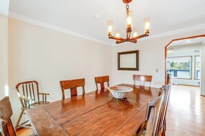 A dining room with a wooden table, six chairs, a chandelier, and a large window.