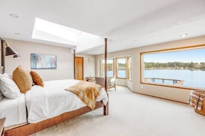 A bedroom with a large bed, a skylight, a view of a lake, and a window with a view of a dock.