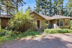 A two-story building with a front porch, surrounded by dense greenery and trees. - Stunning Waterfront Home on Lopez Island with Private Beach Access and Fire Pit (Lopez Island)