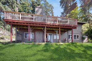A two-story house with a balcony, a chimney, and a grassy yard. - Stunning Waterfront Home on Lopez Island with Private Beach Access and Fire Pit (Lopez Island)