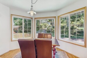 A dining area with a table and chairs, large windows, and a hanging light fixture. - Stunning Waterfront Home on Lopez Island with Private Beach Access and Fire Pit (Lopez Island)