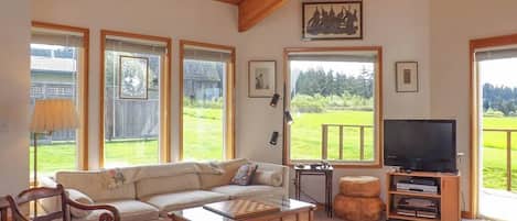 A living room with a wooden ceiling, large windows, a sofa, a coffee table, a television, and a fireplace.
