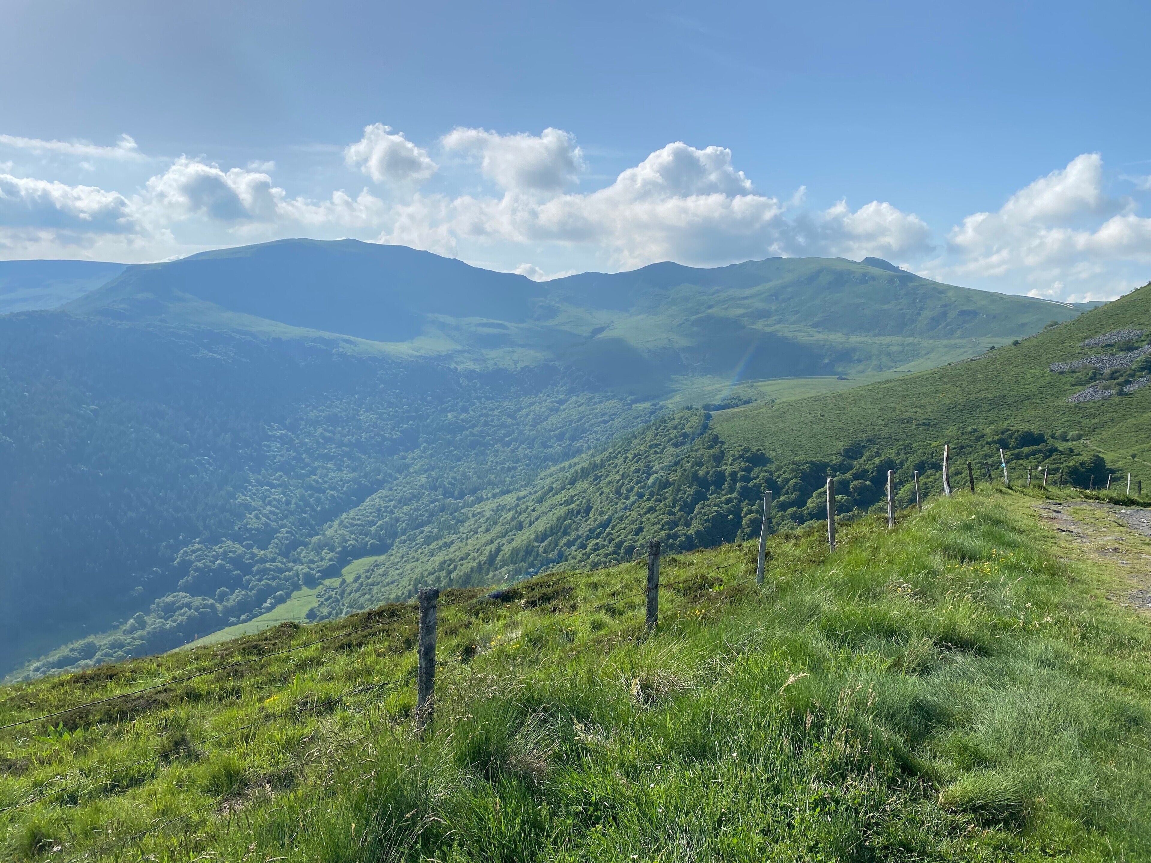 Paisagem montanhosa com primeiro plano gramado e uma cerca.