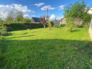 A grassy backyard with a hedge, a tree, and a stone building.