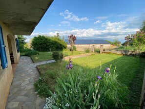 Un sendero de piedra lleva a una casa con techo azul, rodeada por un jardín cuidado con diversas plantas y flores.