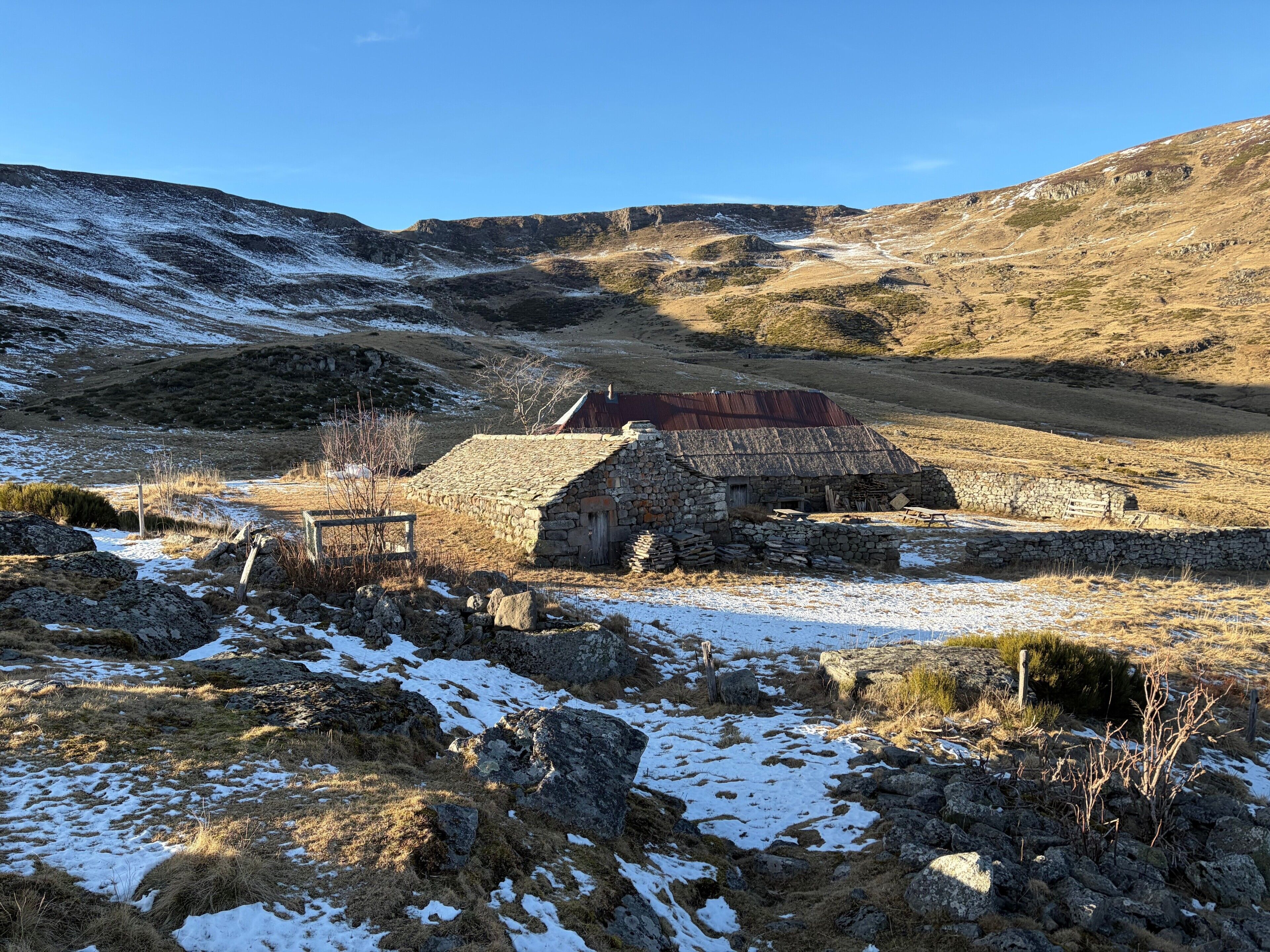 Un bâtiment en pierre coiffé d’un toit rouge, entouré d’un paysage rocheux parsemé de plaques de neige.