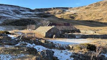 Un bâtiment en pierre coiffé d’un toit rouge, entouré d’un paysage rocheux parsemé de plaques de neige.