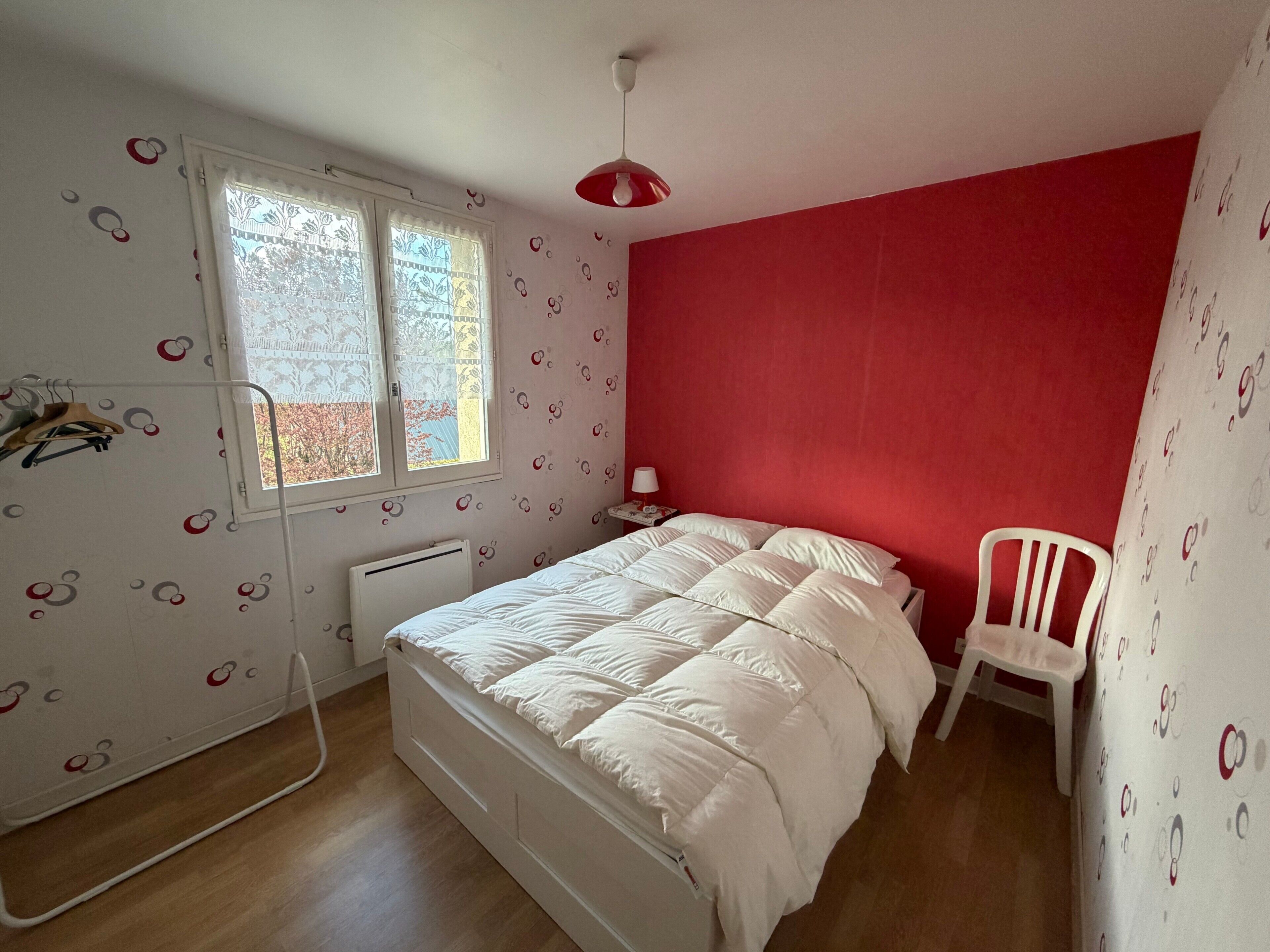 Una camera da letto con un letto, una sedia, una finestra e un termosifone.