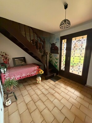 Una escalera que conduce a un segundo piso, un comedor con mantel a cuadros rojo y blanco, un jarrón con flores y un mural en la pared.