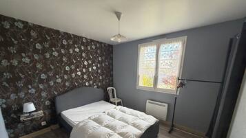 A bedroom with a bed, a chair, a radiator, and a window with curtains.