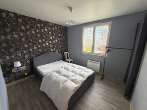 A bedroom with a bed, a chair, a radiator, and a window with curtains. - Country Cottage Near Pierrefort and Col de Prat de Bouc (Cézens)