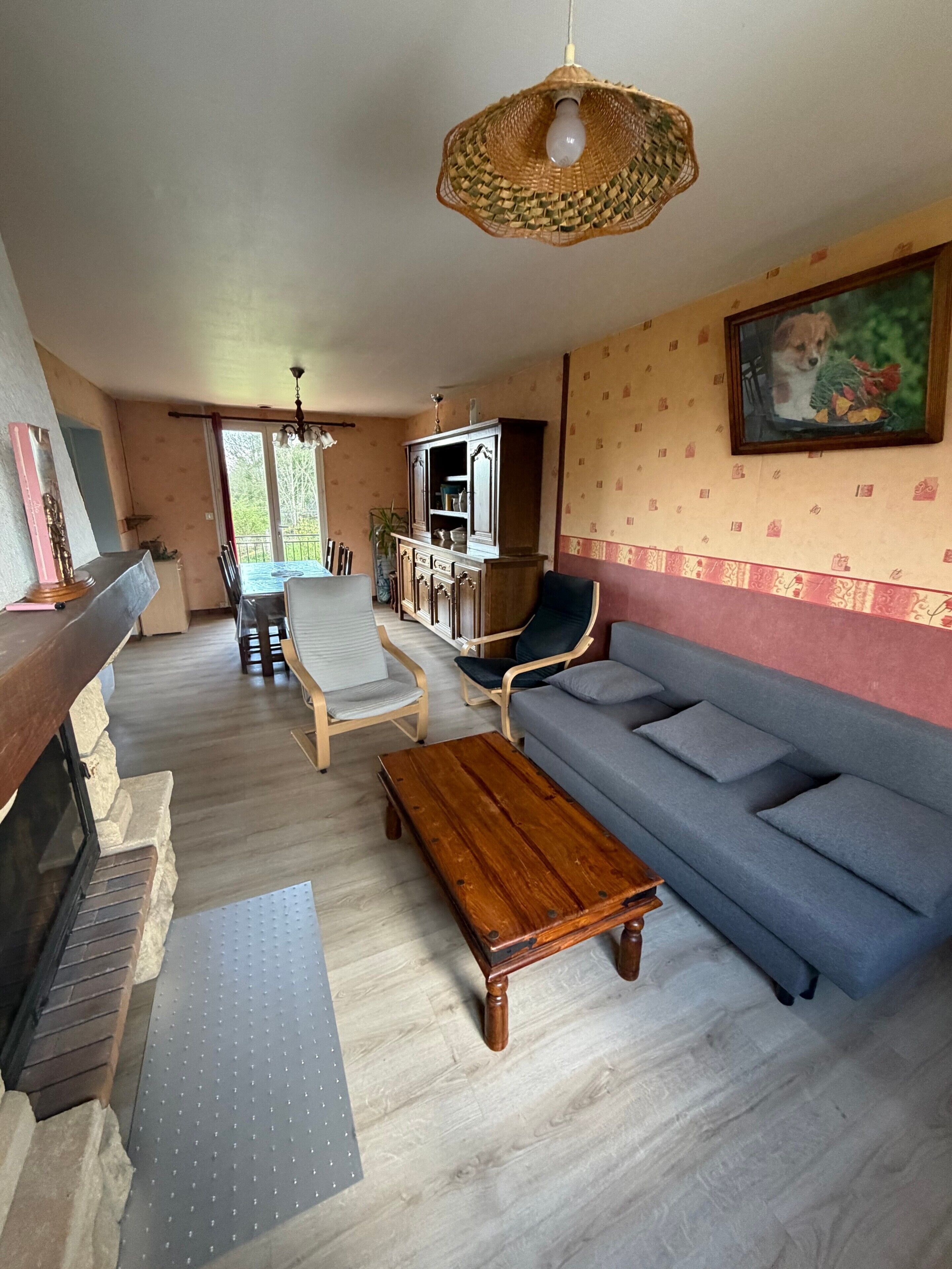 A spacious living room with a wooden coffee table, a grey sofa, and a dining area with a table and chairs.
