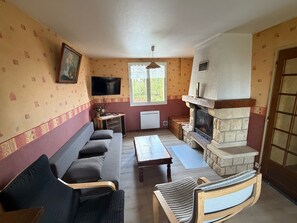 A living room with a sofa, armchair, fireplace, television, and a window.