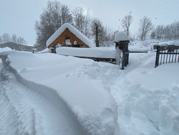A snow-covered landscape with a wooden structure, possibly a barn, and a metal gate.