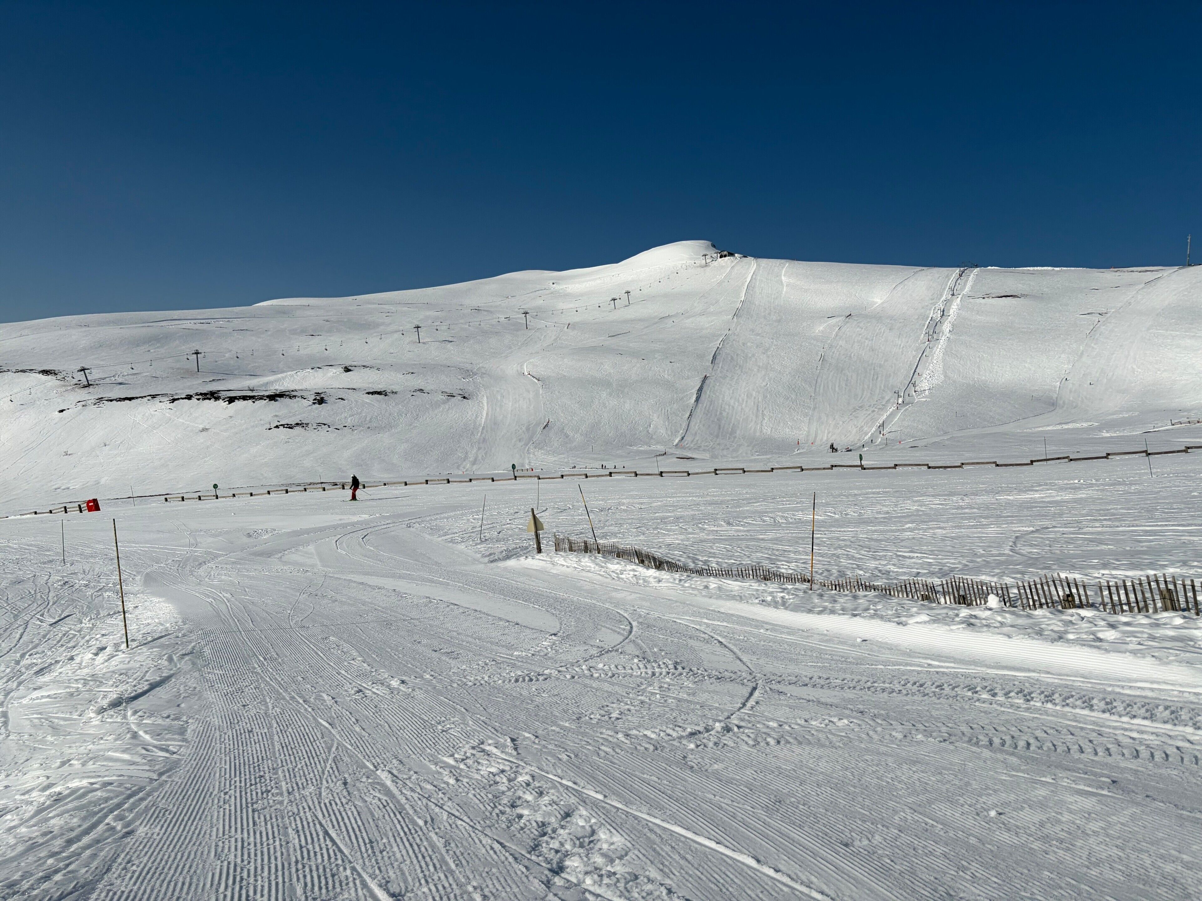 Een piste bedekt met sneeuw, met uitgestippelde loipes en een heldere lucht.