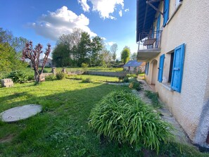Un patio con un sendero de piedra, un área con césped y un edificio con persianas azules.
