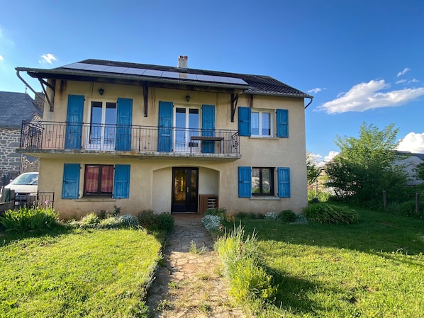 A two-story house with a stone facade, a balcony with metal railings, and a paved driveway leading to the entrance. - Country Cottage Near Pierrefort and Col de Prat de Bouc (Cézens)