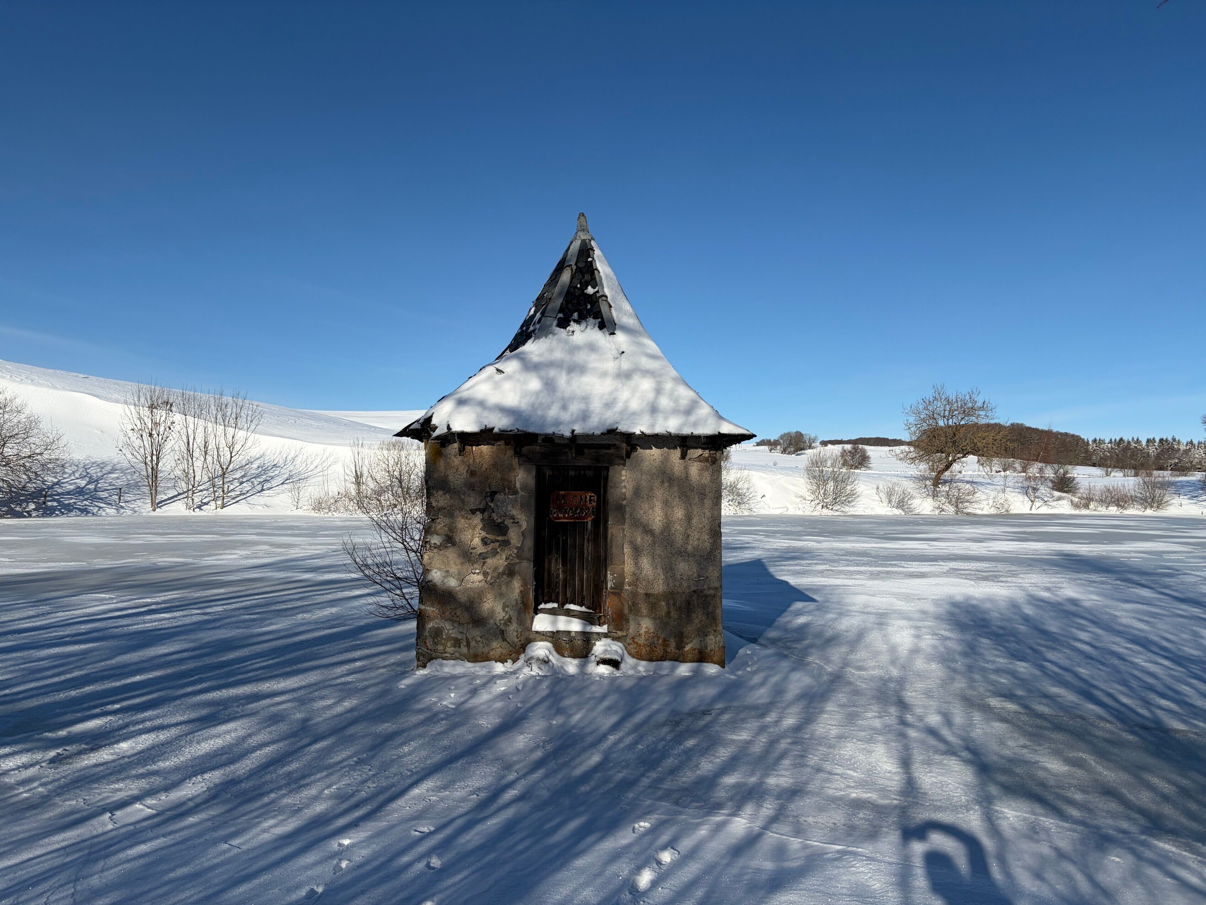 A small, snow-covered building with a steep roof, situated in a snowy landscape.