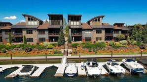 A waterfront property with multiple boats docked, a well-maintained garden, and a modern building with balconies. - Vesper Bleu  2 Kings + EV Charger (Coeur d'Alene)