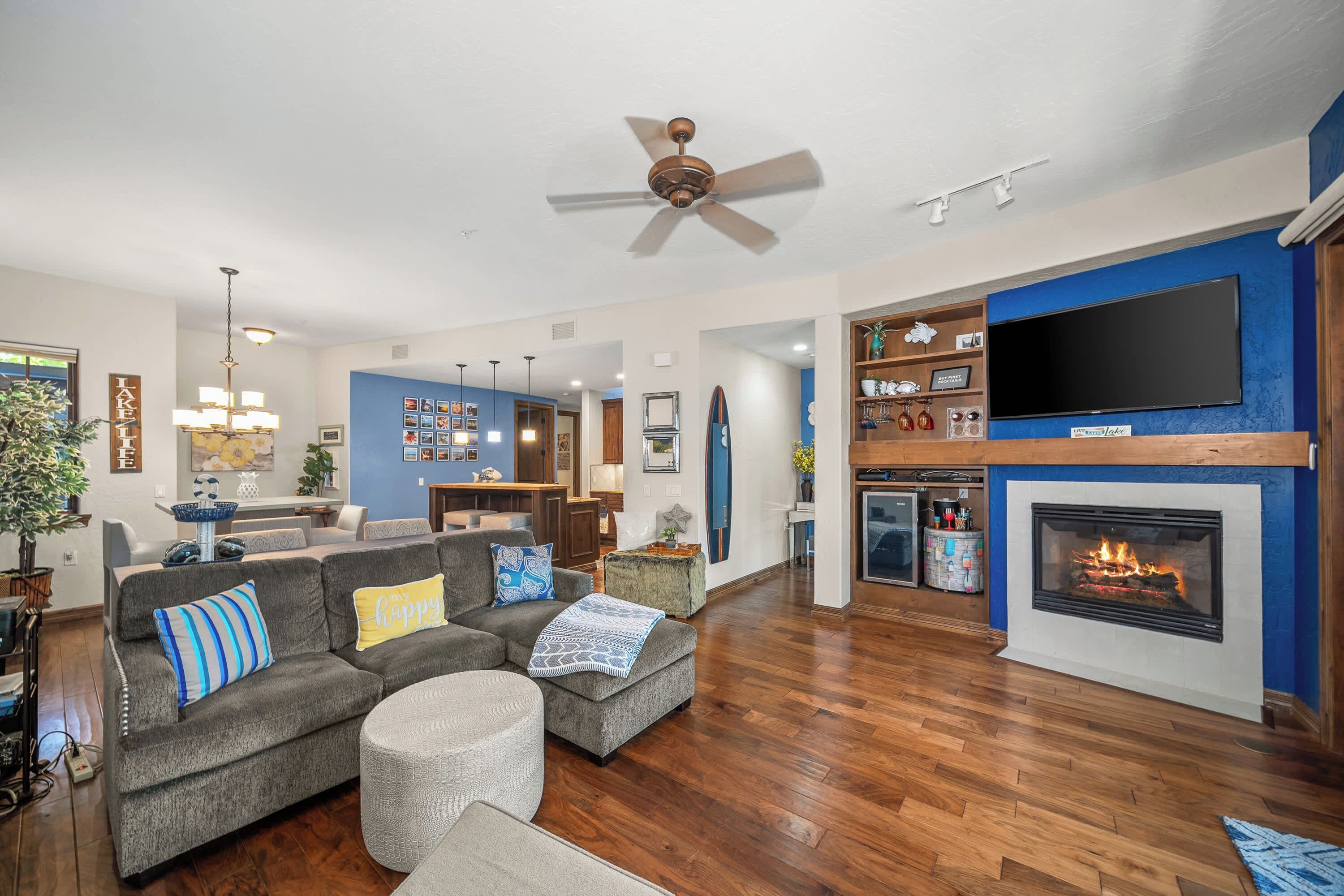 A spacious living room with a fireplace, a television mounted on the wall, and a ceiling fan.