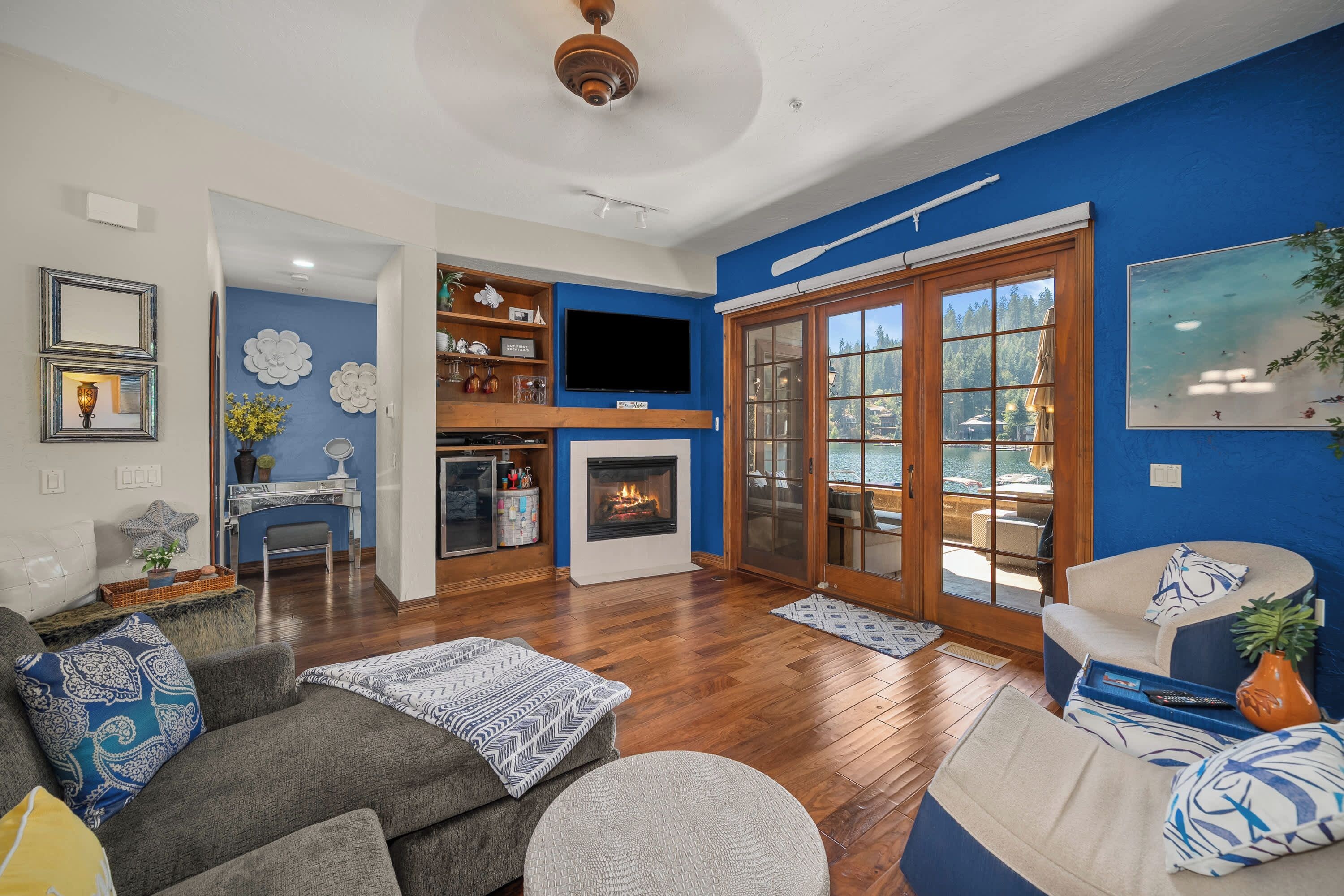 A living room with a fireplace, a television, and a view of a body of water through a glass door.