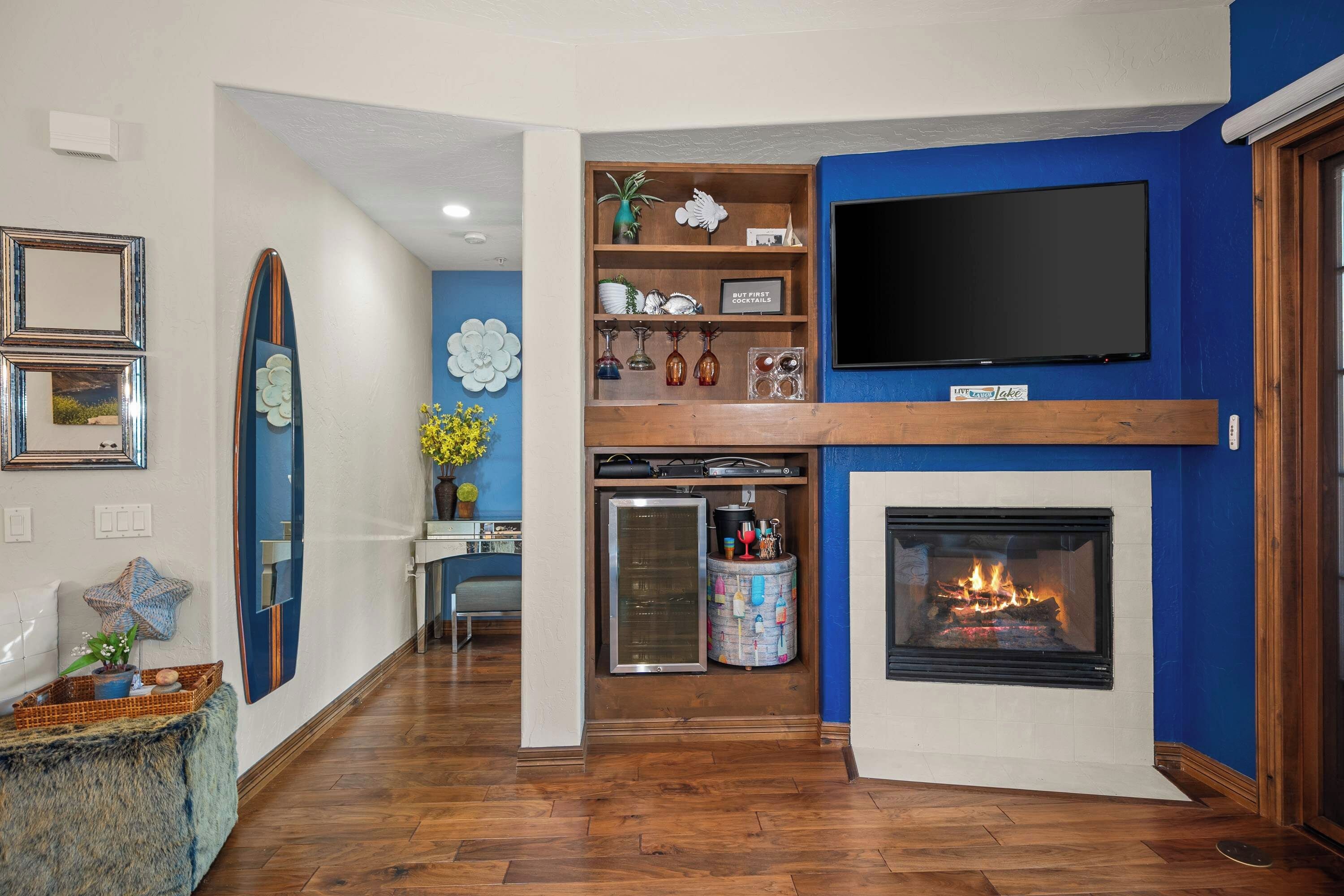 Un salon avec une cheminée, un téléviseur fixé au mur et une décoration murale représentant une planche de surf.