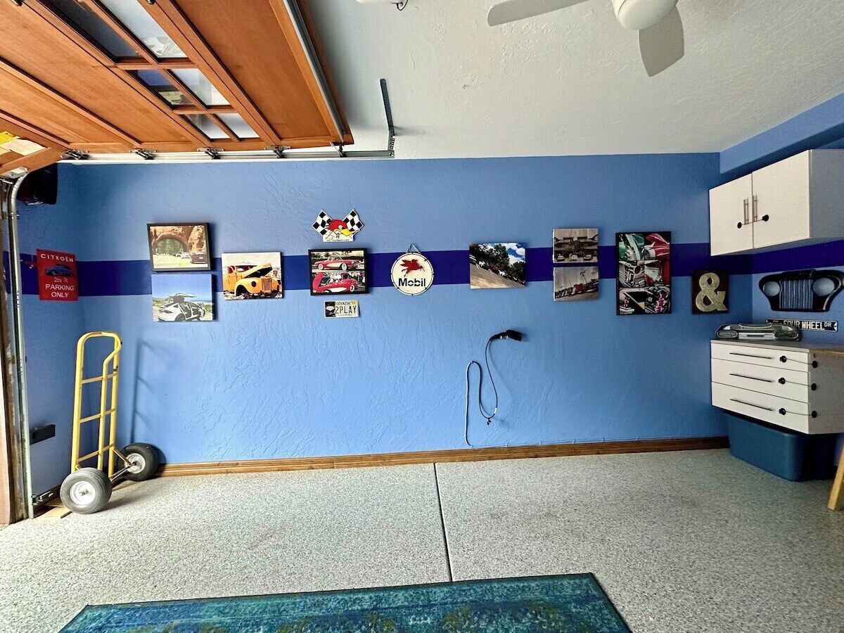 Une pièce avec un mur bleu, une armoire blanche, un bureau et une chaise. Il y a des tableaux accrochés au mur et une échelle dans un coin.