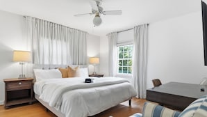 A hotel room with a bed, bedside tables, a desk, a chair, a ceiling fan, and a window with curtains. - 
The Bishop Retreat  5BR, Tennis Court & Yard (Alexandria)