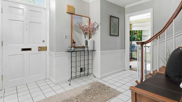 A hallway with a white door, a console table with a mirror and vase, a staircase with a wooden handrail, and a tiled floor. - 
The Bishop Retreat  5BR, Tennis Court & Yard (Alexandria)