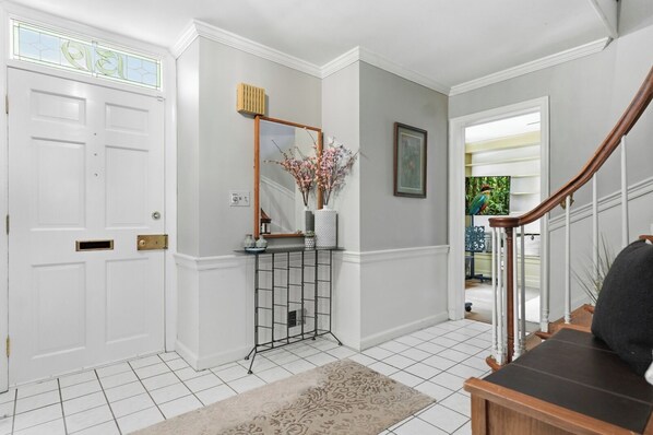 A hallway with a white door, a console table with a mirror and vase, a staircase with a wooden handrail, and a tiled floor. -
The Bishop Retreat 5BR, Tennis Court & Yard (Alexandria)