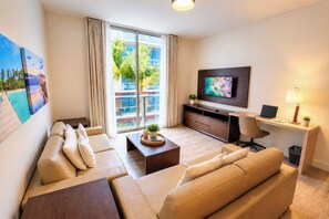 A modern living room with a sofa set, a coffee table, a TV, and a desk with a lamp. - Special Apartment 6 pax with den beachfront (Hollywood)