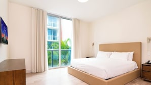 Ein Hotelzimmer mit einem großen Bett, einem Holztisch, einem Nachttisch und Blick auf Palmen.