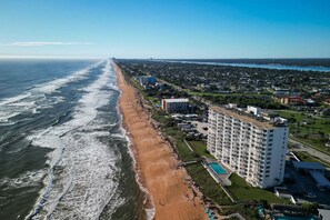 Een hotel aan de kust met een uitgestrekt strand, een zwembad en een parkeerplaats.