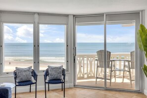 A room with a view of the beach, two chairs, a table, and a sliding glass door. - New Listing! Updated Oceanfront 2/2 | Heated Pool & Garage Parking (Ormond Beach)