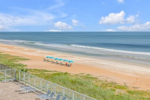 A beach with rows of sun loungers and umbrellas, a clear sky, and calm sea. - New Listing! Updated Oceanfront 2/2 | Heated Pool & Garage Parking (Ormond Beach)