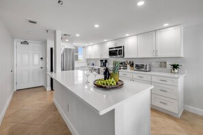 Een moderne keuken met witte kasten, een groot eiland met een fruitschaal, en een ingebouwde magnetron.