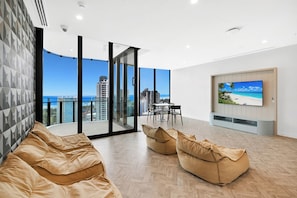 Ein modernes Wohnzimmer mit großem Fernseher, einer Couch und einem Balkon mit Blick auf die Stadt.