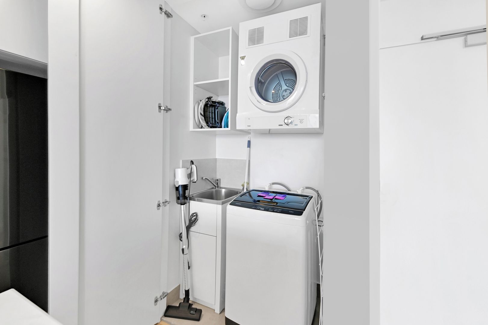 Uma lavanderia compacta com máquina de lavar, pia e aspirador de pó.