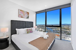 Ein modernes Schlafzimmer mit einem großen Bett, Blick auf die Stadt und einem Bild an der Wand.