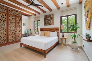 Een slaapkamer met een houten bed, een plafondventilator, een Boeddha-schilderij en een groot raam.